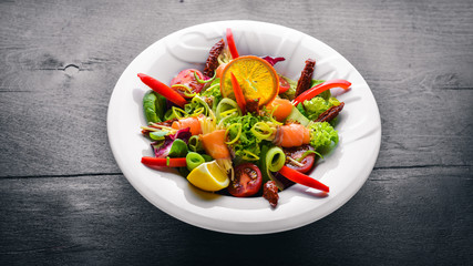 Salad with salmon and fresh vegetables and herbs. Italian cuisine. Top view. On Wooden background.