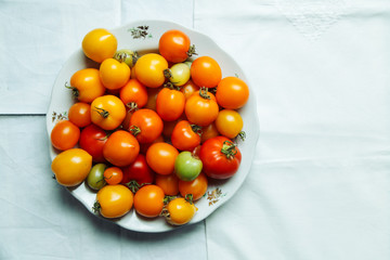 Fresh organic tomatoes of different colors on white textile background. Harvest concept. Horizontal composition. Overhead view, natural lighting, copy space.