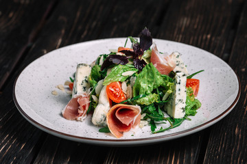Green salad with prosciutto and blue cheese on dark wooden background