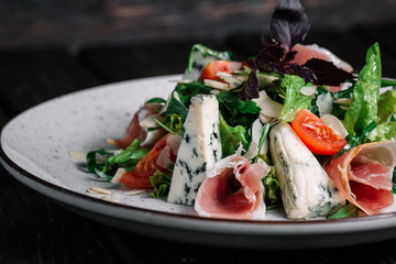 Green salad with prosciutto and blue cheese on dark wooden background