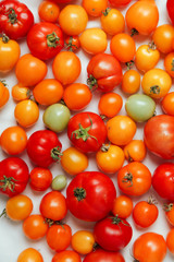 Fresh organic tomatoes of different colors on white textile background. Harvest concept. Overhead view, natural lighting, copy space.