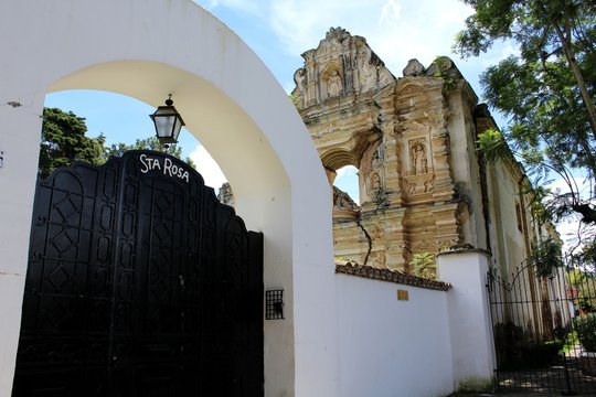 La chiesa Santa Rosa da Lima con il suo portone nero incorniciato da un muro bianco e sul lato enormi alberi. Antigua, Guatemala