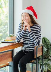 Asian teenage girl with Christmas hat and smile face resting her chin on her hands and drink coffee near window in xmas party at cafe ,Celebrate New year and Christmas holiday concept.