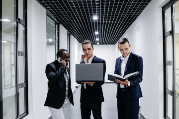 Fototapeta premium Three businessman standing in modern office with laptop and Notepad
