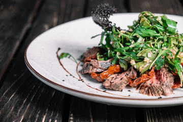 Salad with warm veal, sun-dried tomatoes and arugula on dark wooden background
