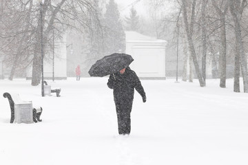 Bad weather in winter: a heavy snowfall and blizzard in city. Male pedestrian hiding from the snow under umbrella