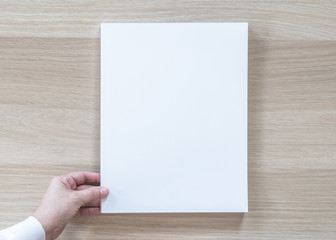 Fototapeta premium Blank A4 size book cover mockup template top view in businessman's hand with page front side on white surface flat lay on wood table