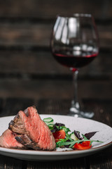 Grilled beefsteak with glass of red wine on dark wooden background