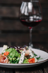 Glass of wine and green salad with prosciutto and blue cheese on dark wooden background