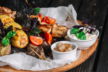 Fototapeta na wymiar Assorted delicious grilled meat with vegetable served with cracklings and brynza on a wooden board on dark wood background
