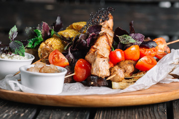 Assorted delicious grilled meat with vegetable served with cracklings and brynza on a wooden board on dark wood background