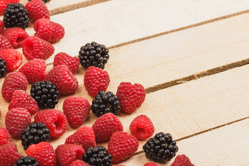 Red raspberries and blackberry on the light wooden background