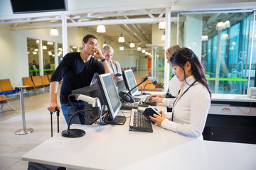 Staff Examining Passport While Passengers Waiting In Airport