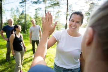 Women Giving High-Five While Friends Standing At Forest