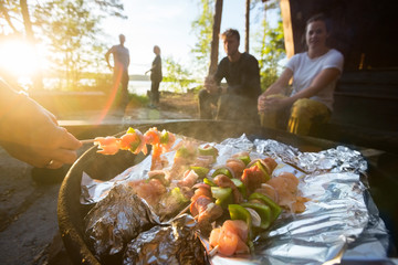 Hand Grilling Food On Skewers With Friends In Background