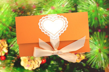 Orange gift envelope tied with a pink ribbon on the background of Christmas tree with cones  