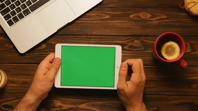 Man swiping pages with his finger on the tablet green screen. Close up. Chroma key. Top view