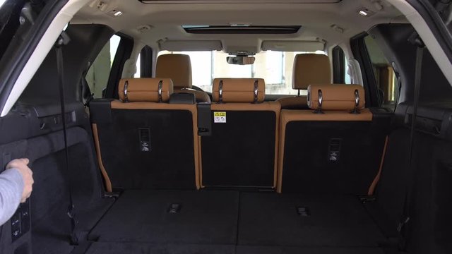 Rear view man demonstrating back seats automatically folding inside mini van vehicle. Automation in contemporary vehicle.