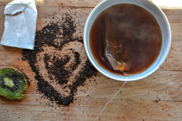 Hot tea in the cup, tea bag, tea powder hearth at the wooden background /top view