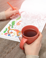 Woman coloring an adult coloring book and drinking tea, new stre