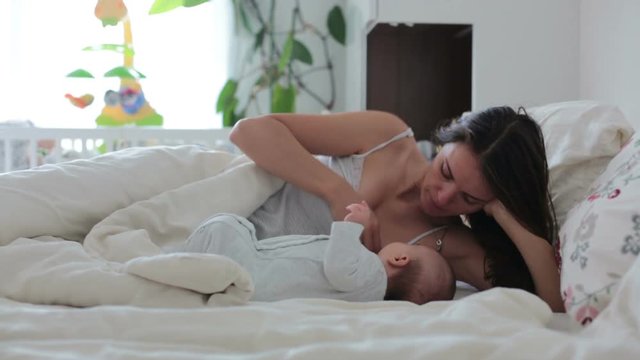 Young mother breastfeeding with her newborn baby boy in bed