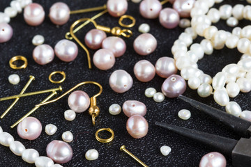 Pearl beads and tools for making jewelry on a black background.