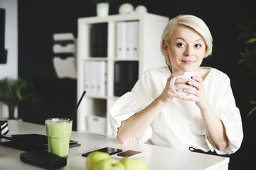 Thoughtful woman sitting at desk and holding mug