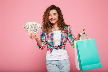 Happy woman with money and shopping bags posing isolated