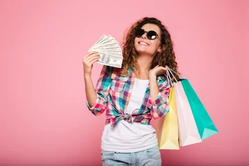 Fotobehang Happy woman with money and shopping bags posing isolated © Drobot Dean