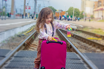 Little girl stay on the rails on railway station.