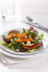Fresh mixed salad on white. Lettuce and arugula leaves with grilled peach and blue cheese.