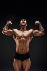 Handsome muscular shirtless man screaming and looking up isolated on black.