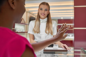 Attractive young woman jewelry store clerc smiling talking to her customer helping her choosing items.