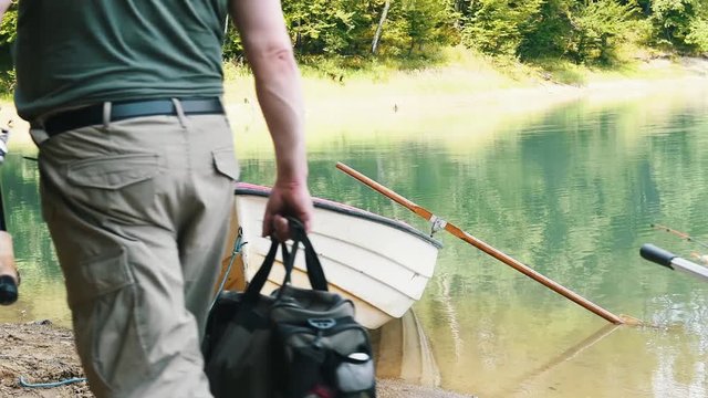 Rear view of men going with fishing rod towards rowboat 