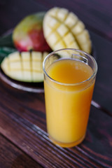 Fresh tropical mango juice on table with mango fruits on background.