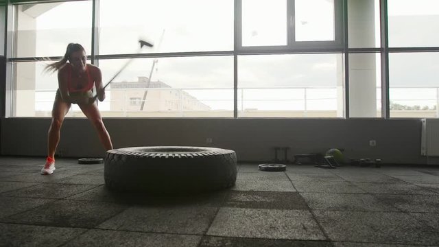 A woman lifts a large tire on an artificial turf field while working out exercising - fitness crossfit exercise workout