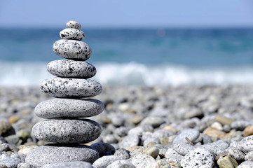 Stones pyramid on pebble beach symbolizing stability, zen, harmony, balance, concept with blur sea background