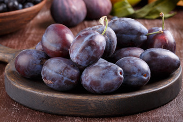 Fresh ripe whole purple damson plums on wooden plate.