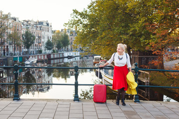 Obraz premium The woman with suitcase is resting on the bridge of Amsterdam city in autumn