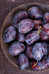Fresh ripe whole purple damson plums on wooden plate.