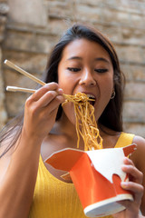 Young asiatic woman eating a chinese take-away on the street