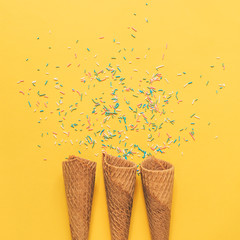 three ice cream cones and confetti on a yellow background