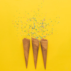 three ice cream cones and confetti on a yellow background. minimal concept of dessert