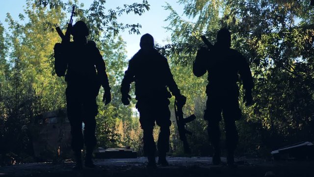 Three dark shapes of armed men walk in to the viewer. 