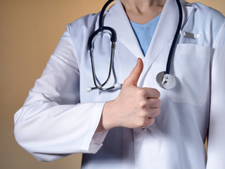 Female doctor showing thumb up. Female doctor with a stethoscope gesticulating on a beige background.