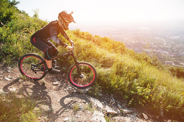 A rider in a helmet is riding along a gravel path from a mountain slope on a mountain bike