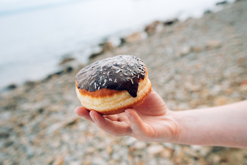 Female hand holding chocolate donut at seaside beach