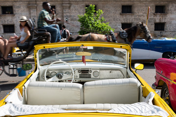 Vintage american yellow car parked and coach passing by in Havana Cuba