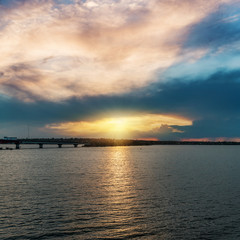 Fototapeta na wymiar sunset in low dark clouds over river with bridge