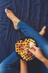 Belgian waffles with cream and frozen raspberries on blue ceramic plate in woman' s hands. Top view